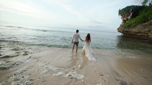 新婚夫妇在傍晚或日落时分在海边的海滩上散步牵手拥抱视频