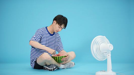 夏日吹风扇吃西瓜的男青年视频