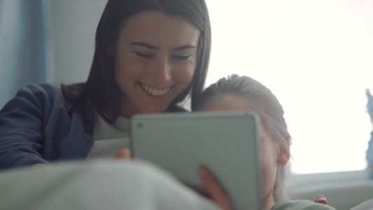 微笑的母亲陪着生病的女儿看平板电脑视频