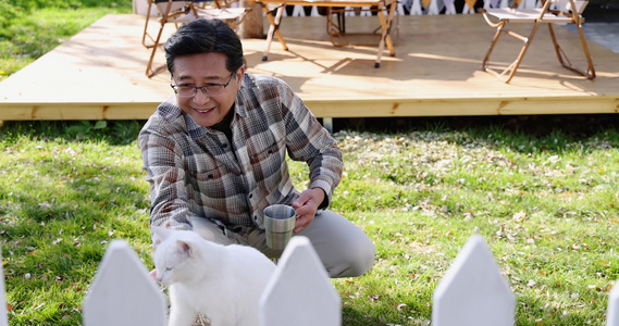 一个老年男人蹲在院子里和猫玩耍视频