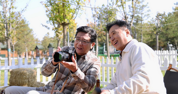 两个老年男人坐在房车露营院子里看数码相机视频