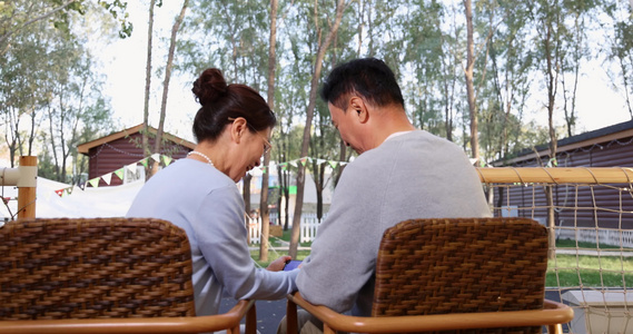 中老年夫妻在露营地坐着摇椅一起看手机聊天视频
