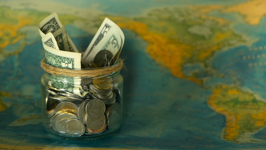旅行预算概念在世界地图背景的玻璃罐中为假期节省的钱视频