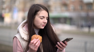 享受汉堡的快乐女人拿着智能手机在城里户外走来走去15秒视频