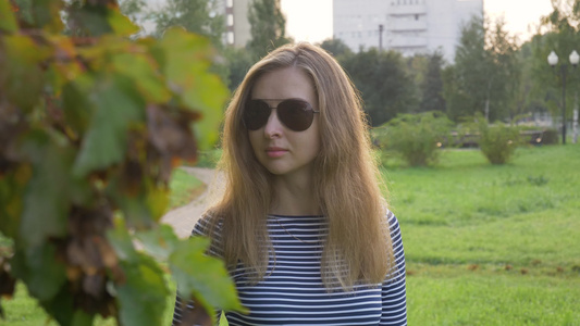戴太阳镜长发的年轻女子在树枝附近走来走去公园视频