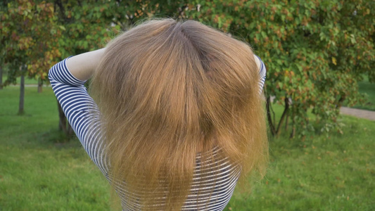 年轻金发女郎在绿公园用手把健康的长发扔了起来超慢动作视频