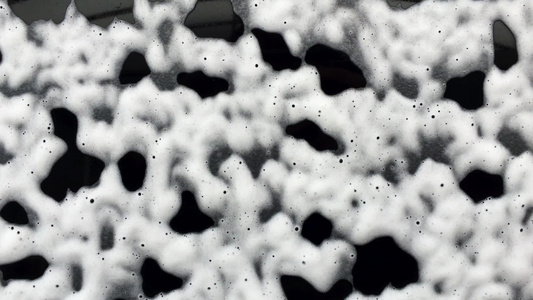 抽象的白色泡沫气泡滑下黑色玻璃洗车香波清洗视频