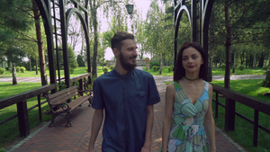 年轻夫妇在公园的一条小路上走在拱门下面聊天和微笑18秒视频