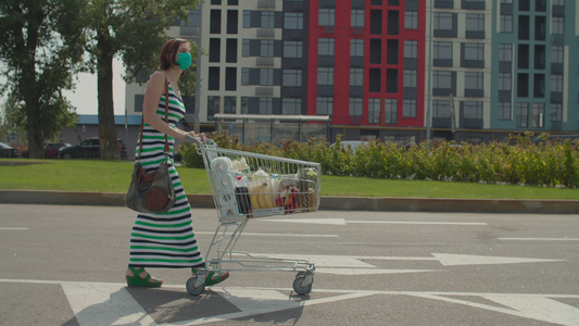 戴着防护面罩的年轻女子带着满满的购物车在购物中心附近视频