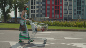 戴着防护面罩的年轻女子带着满满的购物车在购物中心附近25秒视频