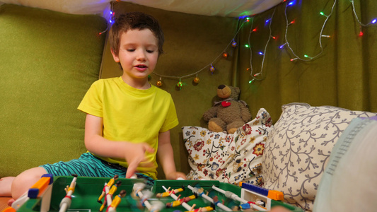 可爱的高加索男孩在有毯子和枕头的小房子里玩桌上足球视频
