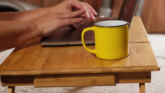 两只女性手和一张笔记本电脑放在木制床边桌子上一个在视频