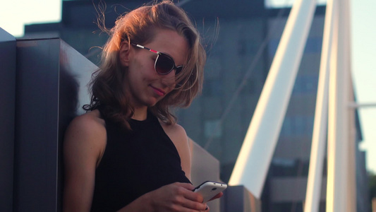 美丽的年轻女孩在桥上摆着一个智能手机听音乐和跳舞的视频