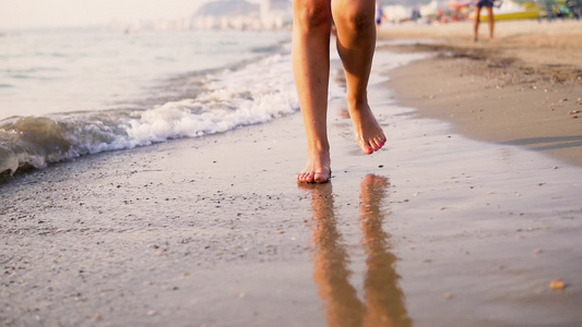 年轻女子的腿踩在海边沙滩上海浪缓慢飘动视频