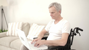 坐在笔记本电脑旁的白发男子坐在他病房里的轮椅上10秒视频