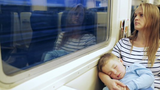 女人看着火车窗外的女人和她儿子睡在大腿上视频