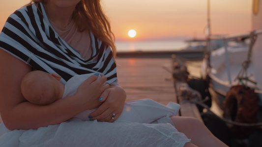 日落时坐在码头的婴儿哺乳和抚育母亲视频