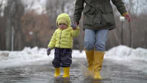 母亲和女儿穿着黄色橡胶靴子在水坑里行走11秒视频