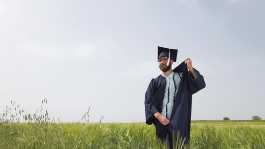 独自在绿色田野毕业的男子脱光衣服和扔下蓝帽子和礼服视频
