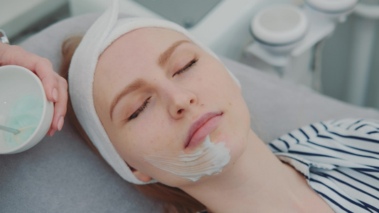 在美容院对年轻女性的脸部涂上奶油面具的化妆手视频