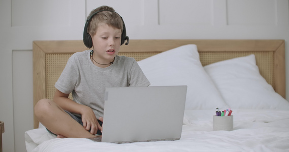 男孩在家里与同学或家长通过笔记本电脑视频聊天头部耳机视频