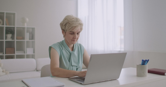中年金发女子在社交网上通过笔记本电脑使用互联网键盘视频