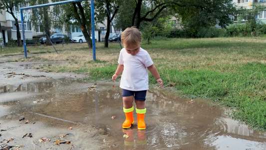 穿着橙色靴子的幼儿在雨后穿过水坑视频