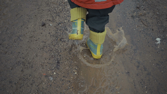 男孩在春天穿过水坑和泥土视频