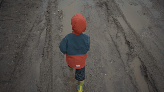 男孩在春天穿过水坑和泥土视频