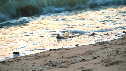 海边日落沙滩上留下塑料玻璃和废物海浪将它们吹入海中视频