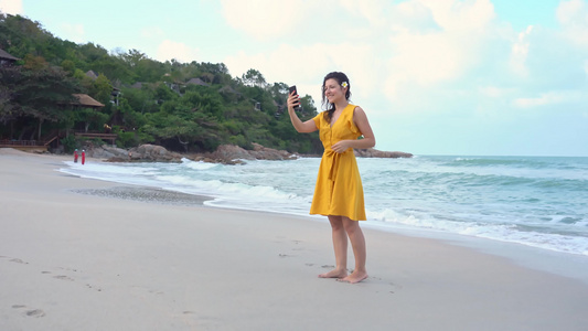 一个穿着黄色裙子的年轻美女带着自拍在电话上沿着海湾视频