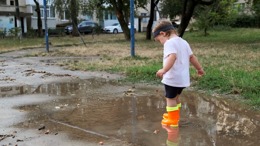 穿着橙色靴子的幼儿在雨后穿过水坑视频