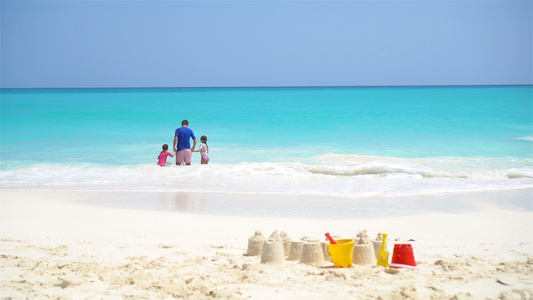白沙滩上的沙堡有塑料小孩玩具和家庭在海背景中视频