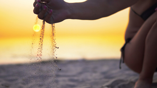 女性模范手在沙滩日落时倾洒沙子暑假的概念视频