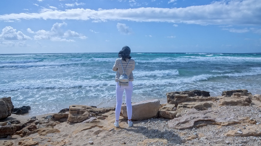一位年轻女子站在暴风海岸的风中望着地平线视频