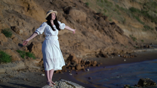 女人旅行者举起双臂看着大海在海上享受草帽和白色连衣裙视频