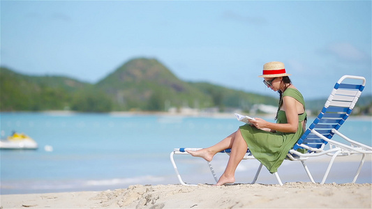 年轻妇女在热带白沙滩上阅读关于日晒的书视频
