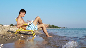 年轻男子在海滩度假时坐在椅子上阅读16秒视频