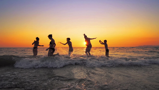 家庭成员在夏日海滩的日落时分欢快跳跃电影慢动作视频