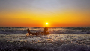 年轻微笑的女人坐在海浪中在日落时分在暑假放松飞溅的14秒视频