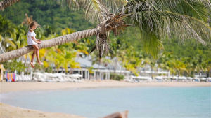 热带沙滩上可爱的小女孩在暑假时坐在棕榈树上15秒视频