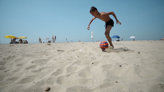 男孩在沙滩上玩雪球踢足球视频