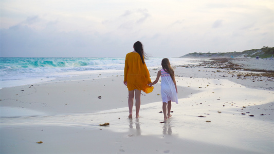 可爱的小女孩和年轻母亲在温暖的夜晚在热带海滩上视频
