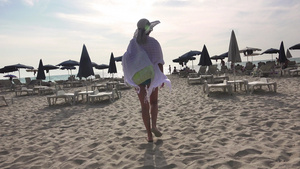 美丽的无忧无虑的女孩在沙滩椅和太阳伞之间沿着海边的22秒视频
