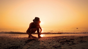 带着帽子的男孩在海滩上寻找一块平板石头27秒视频