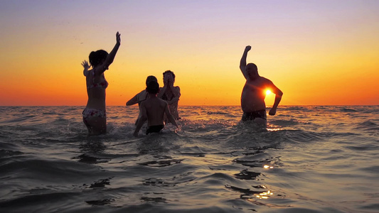 一群家人朋友在日落时游入海中水潮湿喷水拍电影慢动作视频