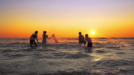 一群快乐的人在日落时在海滩上玩耍和喷水美丽和快乐的视频