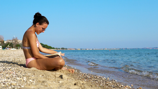 年轻女性在海滩海岸享受假期阅读一本书视频