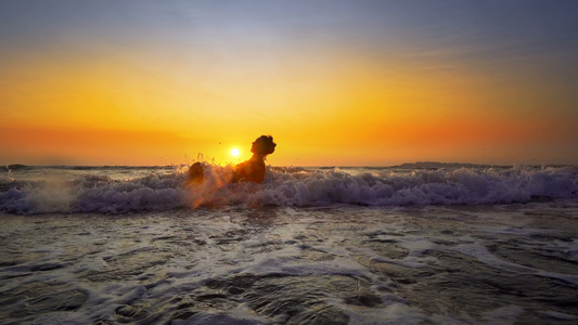 年轻微笑的女士坐在海浪中在日落暑假时放松视频