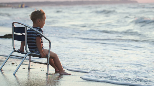 男孩坐在椅子上坐着海边波浪洗脚视频